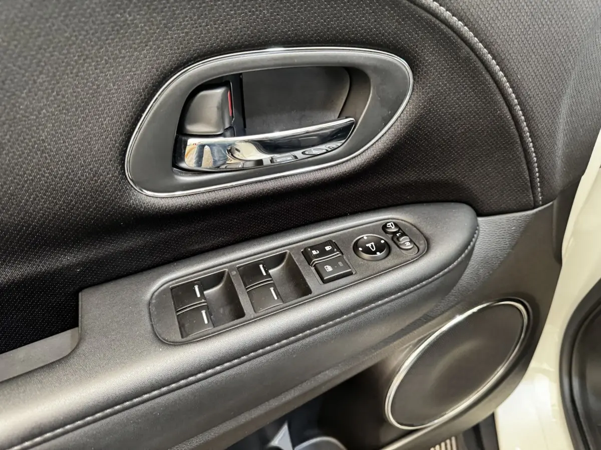 Gros plan sur la porte côté conducteur du Honda HR-V blanc, montrant les commandes des vitres et le haut-parleur rond chromé.