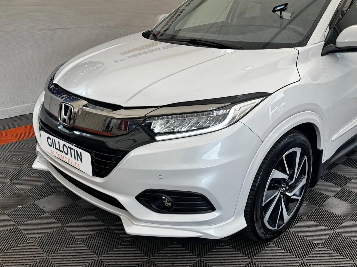 Vue 3/4 avant droit d'un Honda HR-V blanc 2019 avec calandre chromée et jantes alliage noires et argentées.