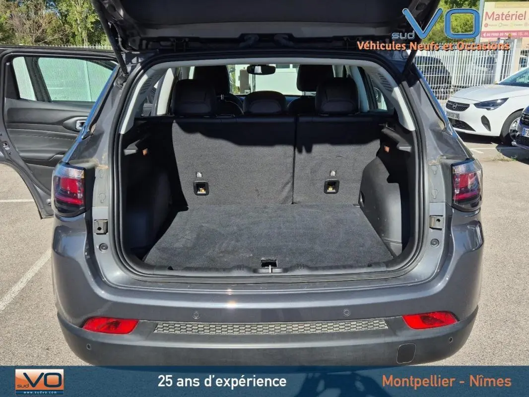 Coffre ouvert en vue arrière d’un Jeep Compass gris 2024 avec hayon relevé et porte arrière gauche ouverte.