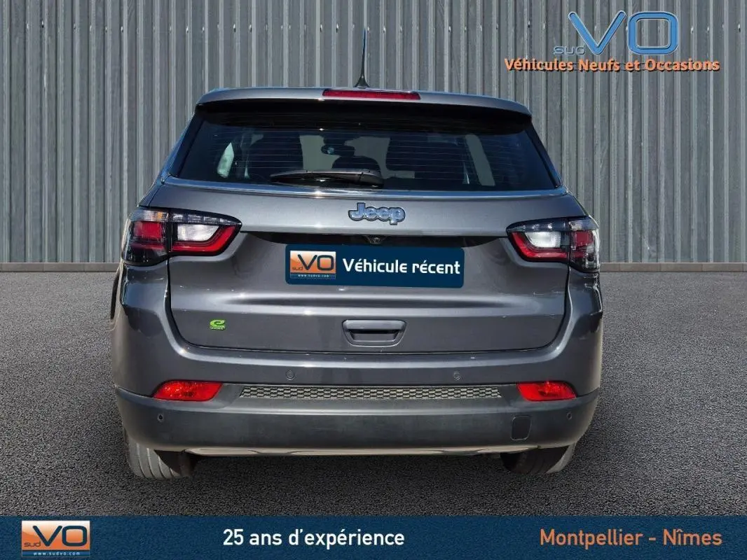 Vue arrière d'un Jeep Compass gris 2024 avec feux LED et logo e-Hybrid visible sur un parking extérieur.