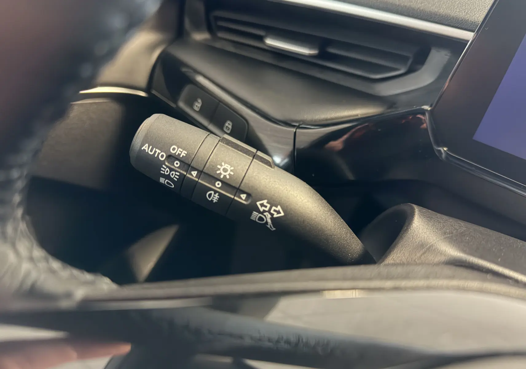 Gros plan sur la commande des feux et clignotants du MG3 1.5 L Hybrid+ 2025, intérieur noir avec écran tactile visible.