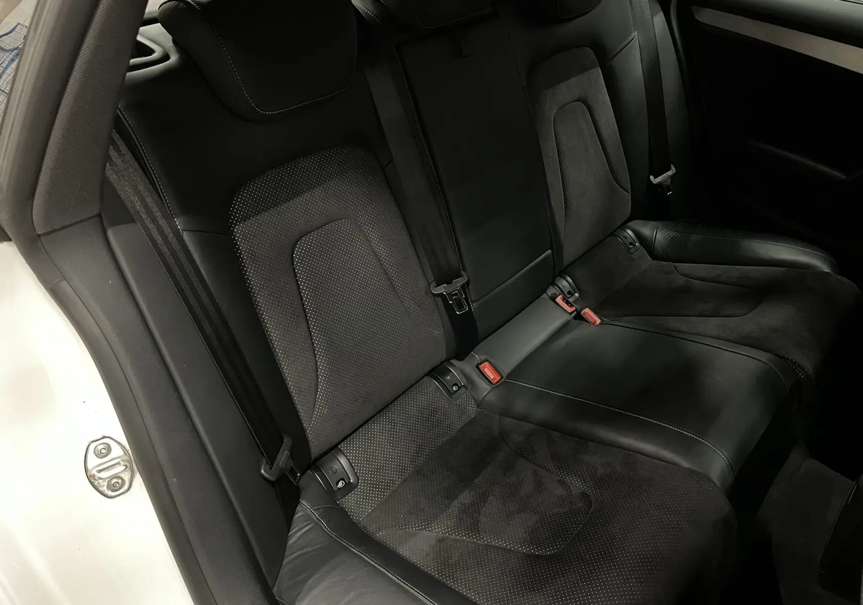 Vue intérieure de la banquette arrière noire en cuir et alcantara de l'Audi A5 Sportback blanche, côté gauche ouvert.