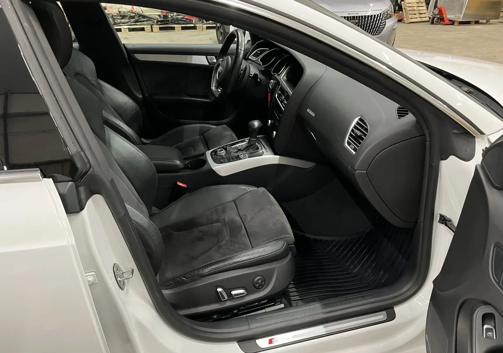 Intérieur côté conducteur d’Audi A5 Sportback blanc 2015, sièges noirs cuir/alcantara et console centrale avec boîte auto.