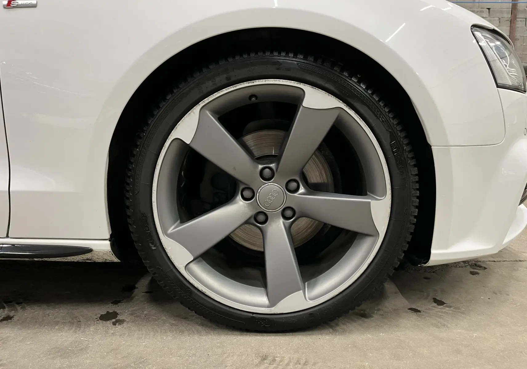 Gros plan sur la roue avant droite de l'Audi A5 Sportback blanche avec jante alliage cinq branches et logo Audi au centre.