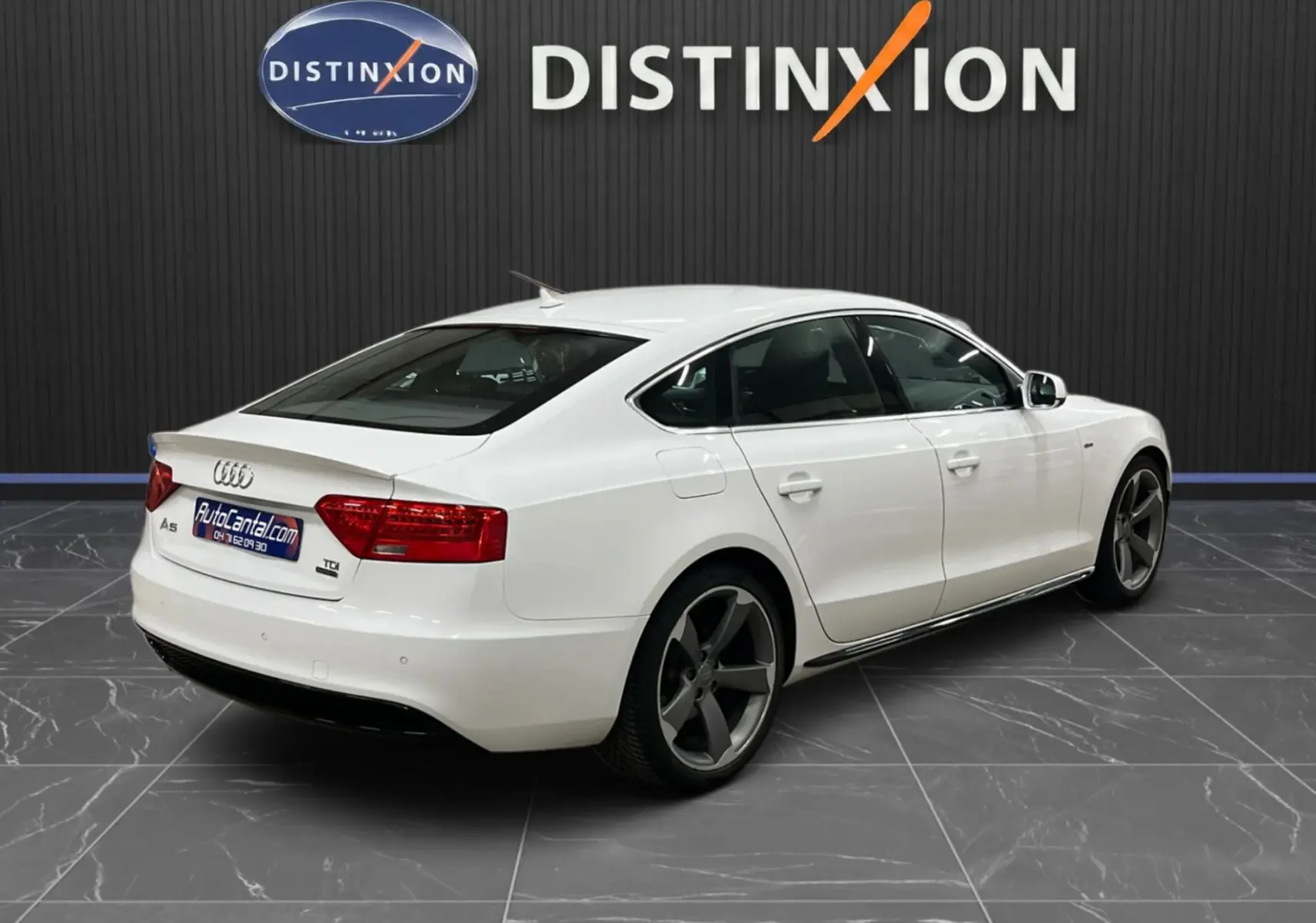 Audi A5 Sportback blanc vue 3/4 arrière droit avec jantes gris foncé dans un showroom intérieur.