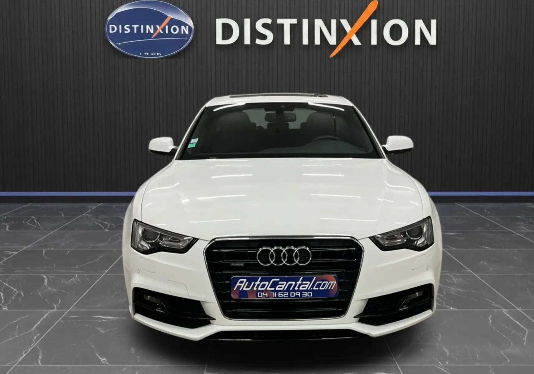 Audi A5 Sportback blanc vue de face dans un showroom avec logo Distinxion en arrière-plan.