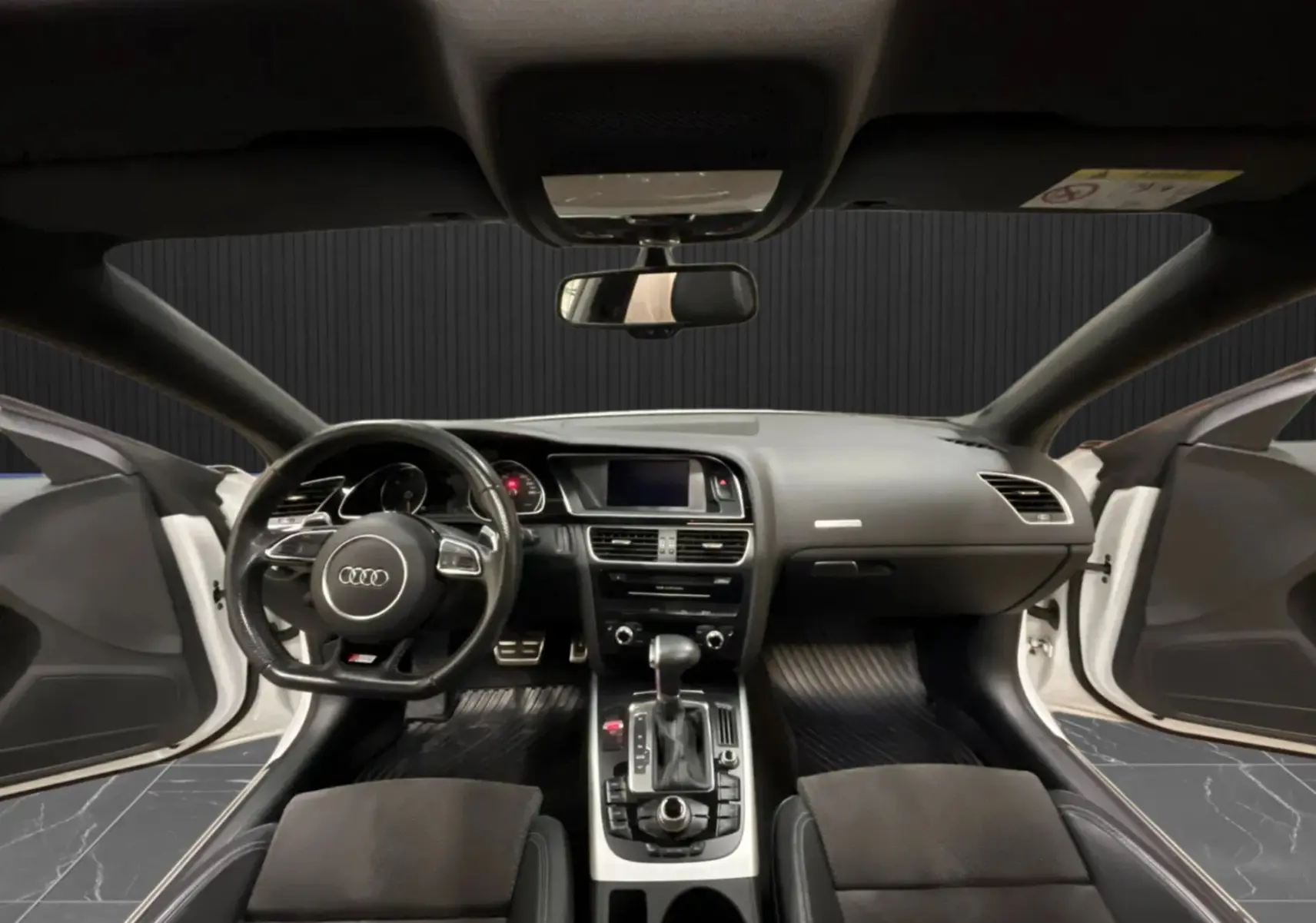 Vue intérieure avant de l'Audi A5 Sportback blanche 2015, tableau de bord et volant avec portes ouvertes.