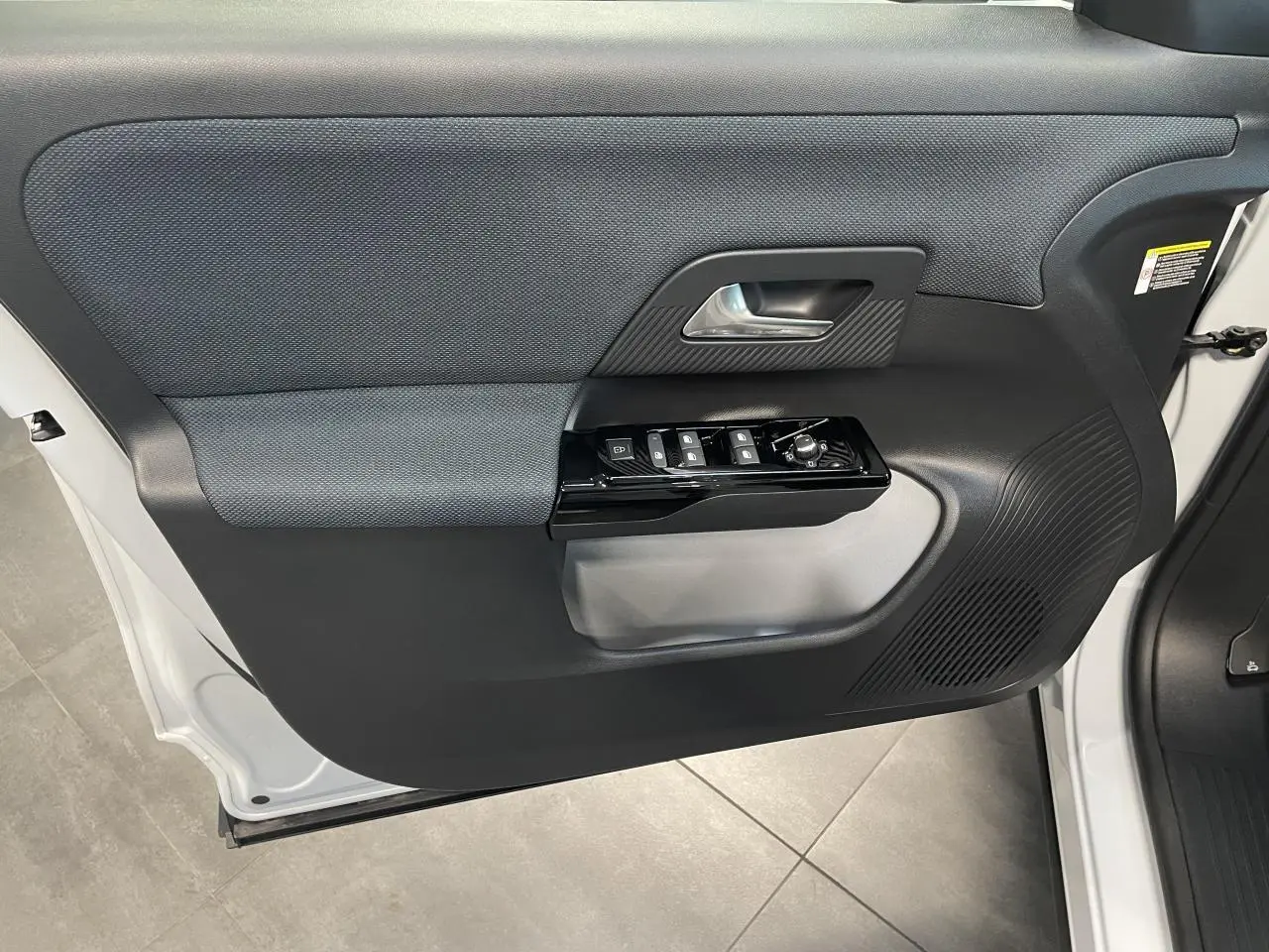 Porte avant gauche ouverte d’un Citroën C5 Aircross blanc, avec panneau intérieur noir et commandes de vitres.