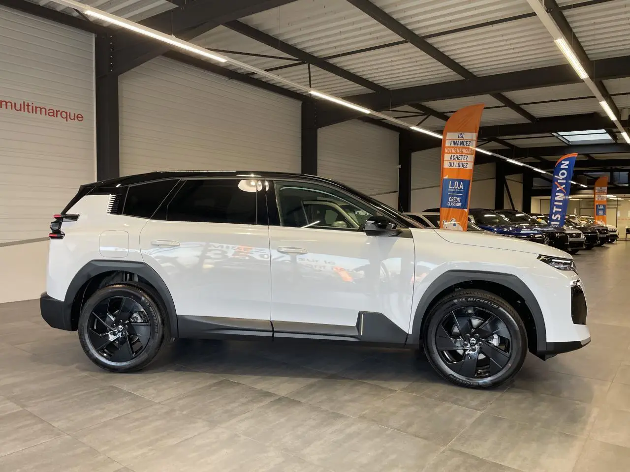 Vue profil droit d'un Citroën C5 Aircross blanc Okenite avec toit noir et jantes alliage noires en showroom.