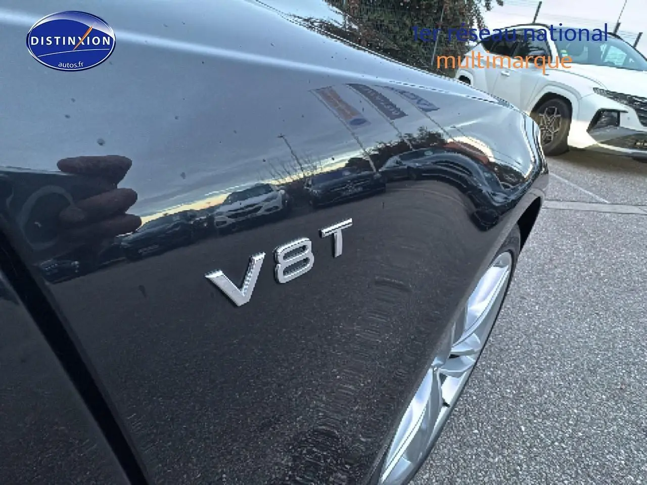 Gros plan sur l'aile avant droite noire d'une Audi S7 Sportback avec l'insigne V8T visible au-dessus de la roue.