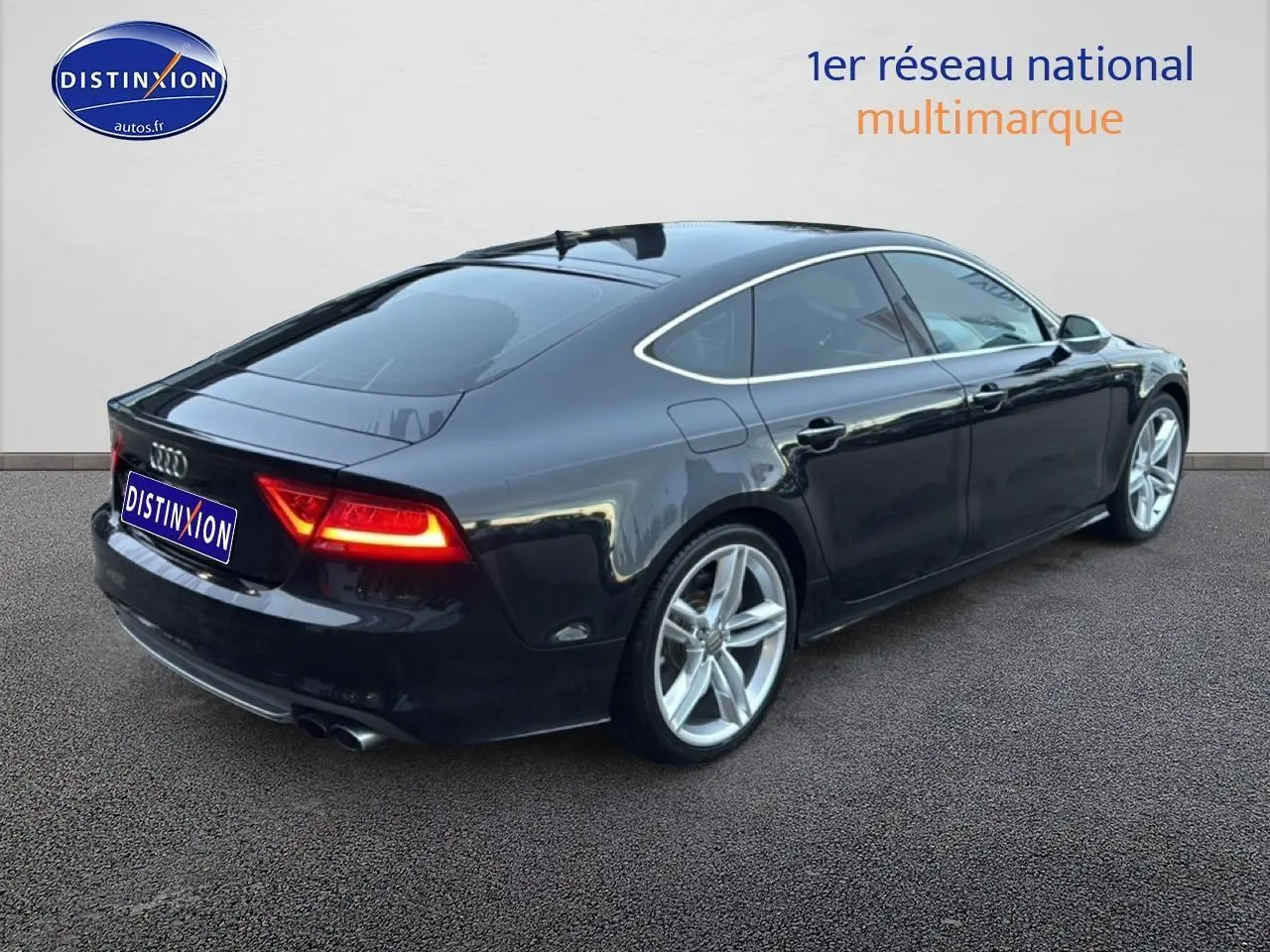 Audi S7 Sportback noir vue 3/4 arrière droit avec jantes alu et feux arrière allumés sur sol gris.