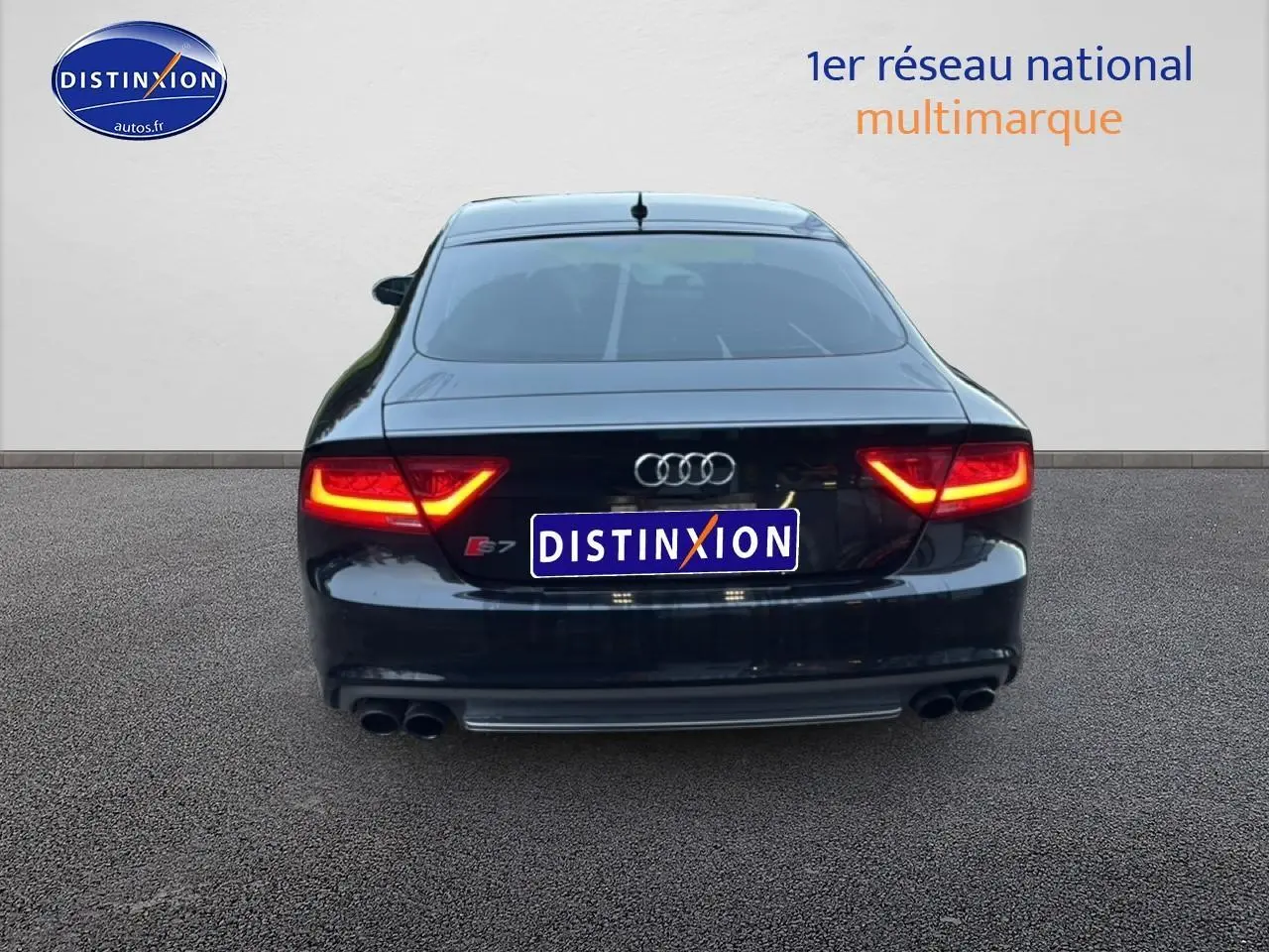 Vue arrière d'une Audi S7 Sportback noire avec feux allumés et double sortie d'échappement chromée.