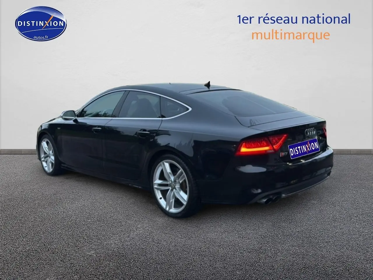 Audi S7 Sportback noir vue 3/4 arrière droit avec jantes alu et feux arrière allumés.