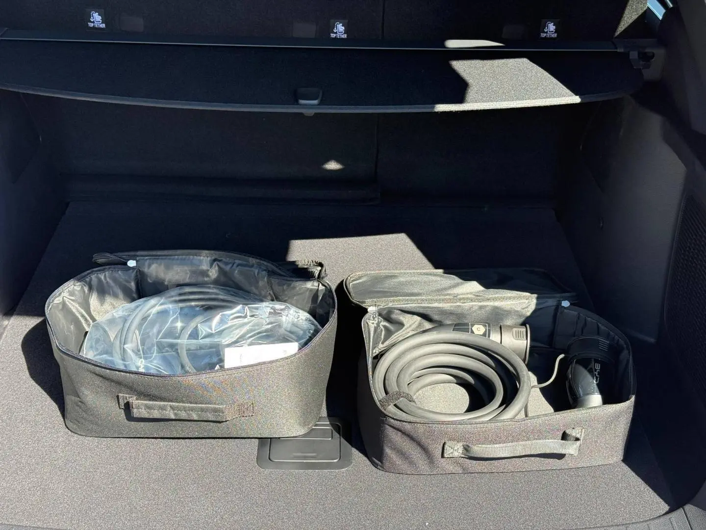 Coffre ouvert d’un BYD SEAL U 1.5 DM-i 324ch Design AWD 2026, montrant les câbles de recharge rangés dans des sacs noirs.