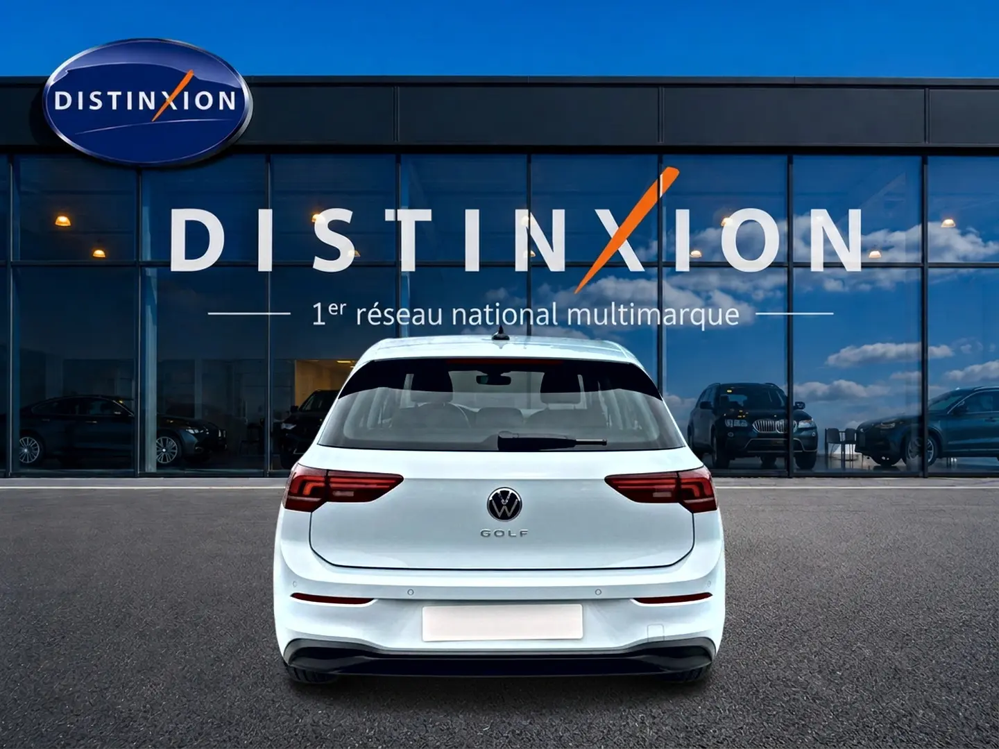 Vue arrière d'une Volkswagen Golf 2026 bleu glacier garée devant une vitrine avec logo Distinxion.