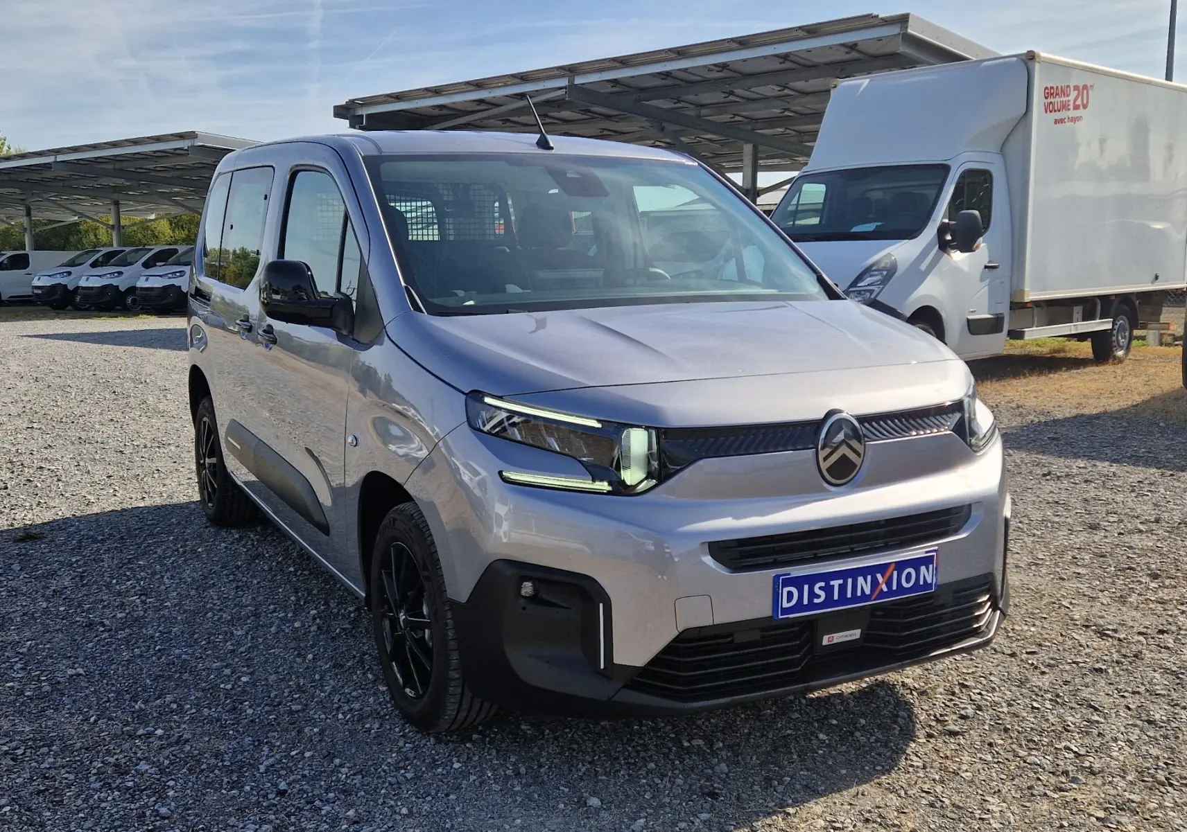 Vue 3/4 avant gauche d'un Citroën Berlingo gris Artense avec calandre noire et jantes noires sur un parking extérieur.