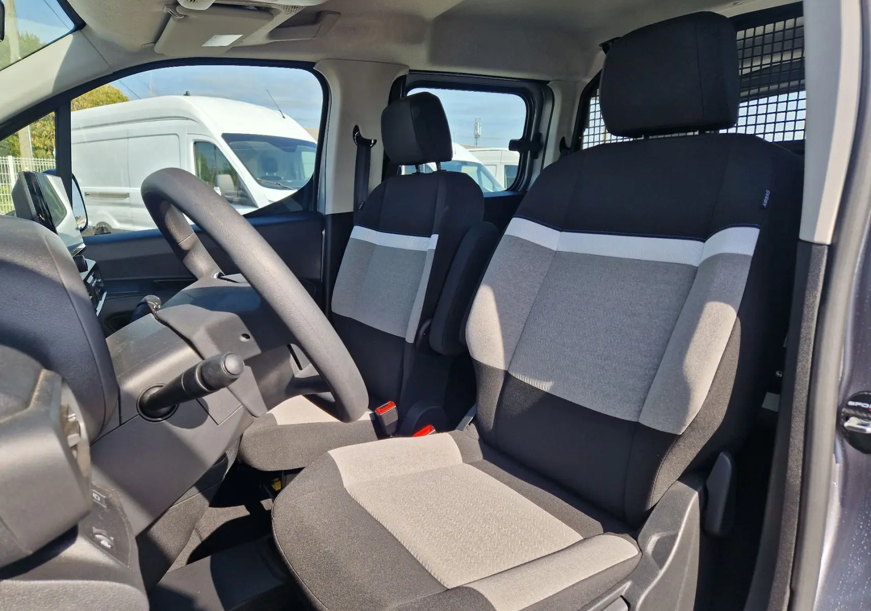 Vue intérieure côté conducteur du Citroën Berlingo gris Artense 2025, sièges bicolores et grille de séparation visible.
