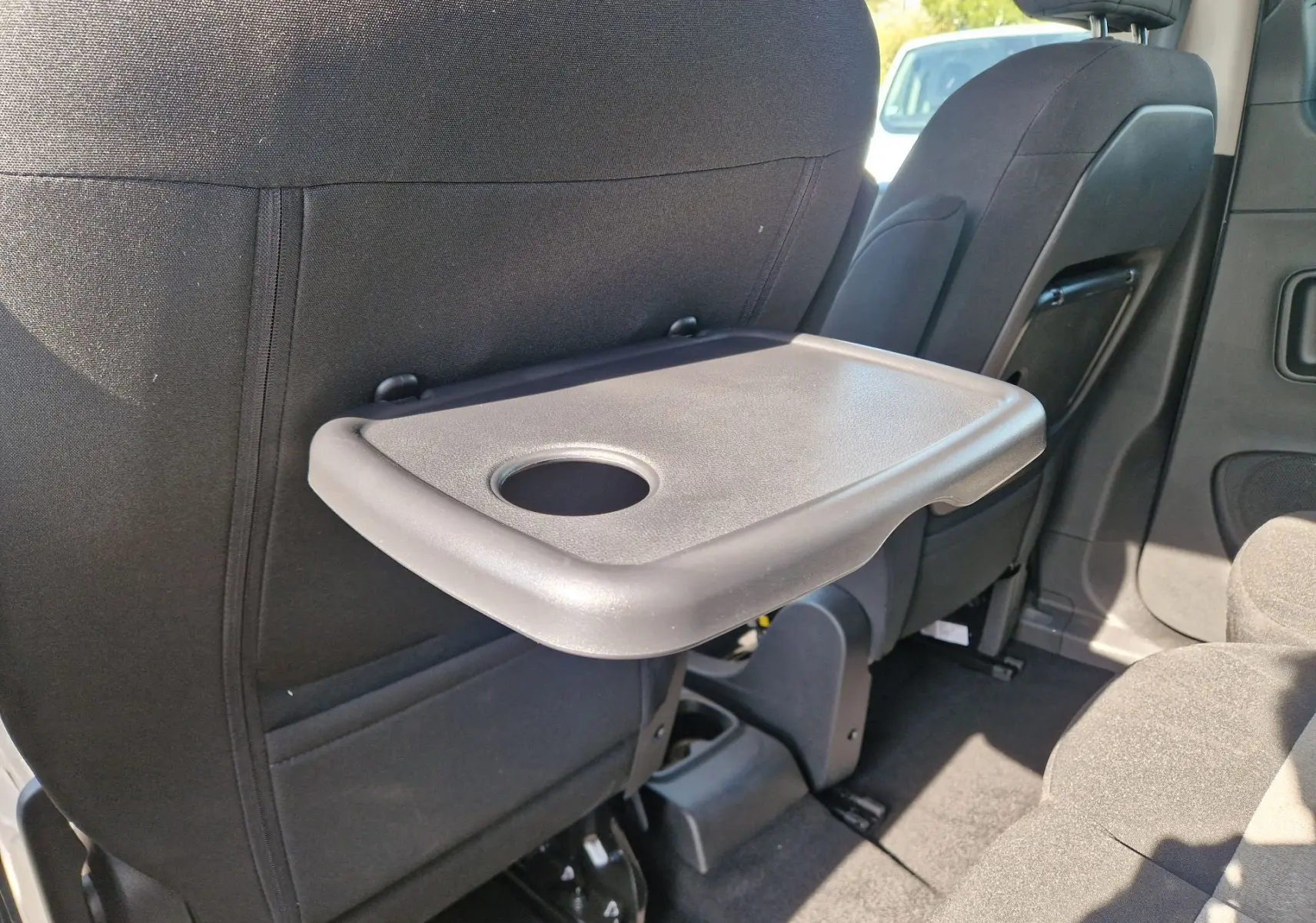 Tablette rabattable avec porte-gobelet fixée au dossier du siège avant droit dans l'habitacle du Citroën Berlingo gris Artense.
