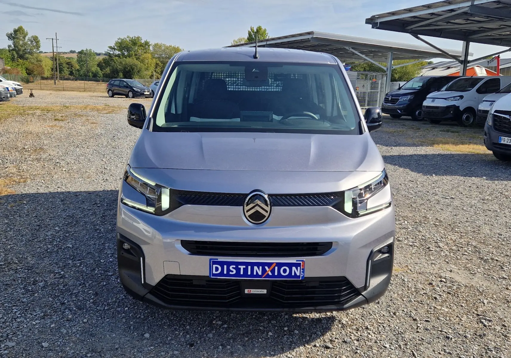 Vue avant d'un Citroën Berlingo gris Artense 2025 avec calandre noire et plaque Distinxion sur un parking extérieur.