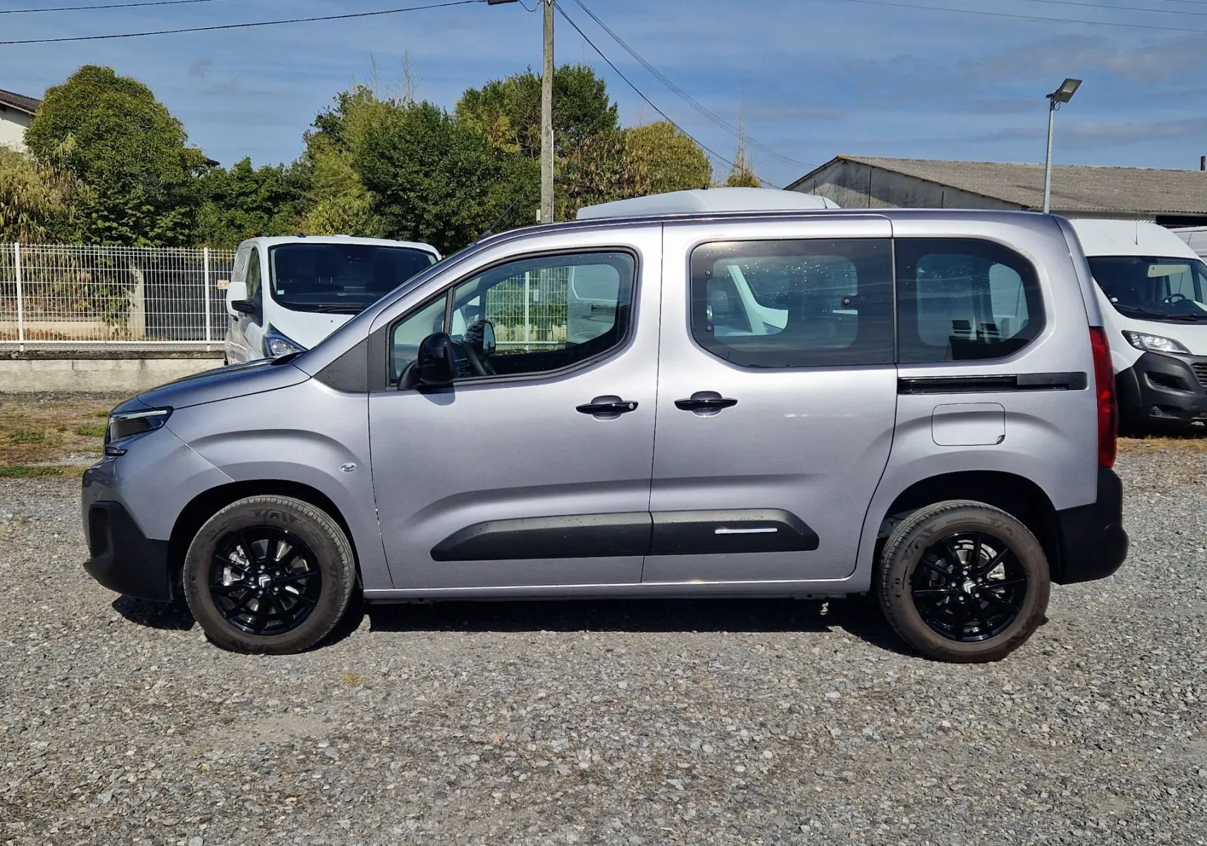 Vue de profil côté gauche d'un Citroën Berlingo gris Artense 2025 avec jantes noires et protections latérales noires.