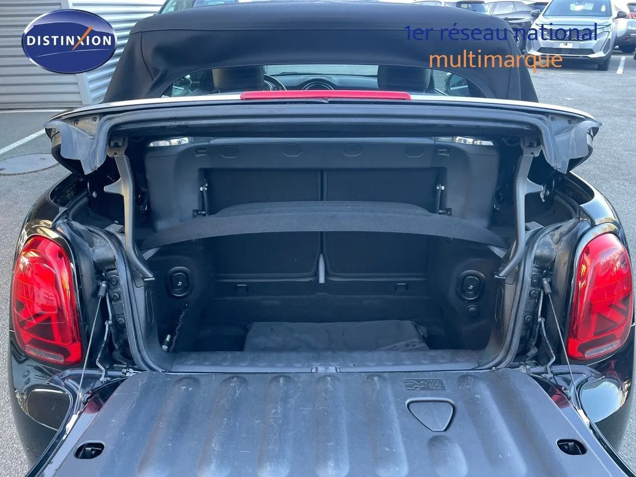Coffre ouvert vu de l'arrière d'une MINI Cabriolet F57 noire, découvrant l'espace de rangement et la capote relevée.