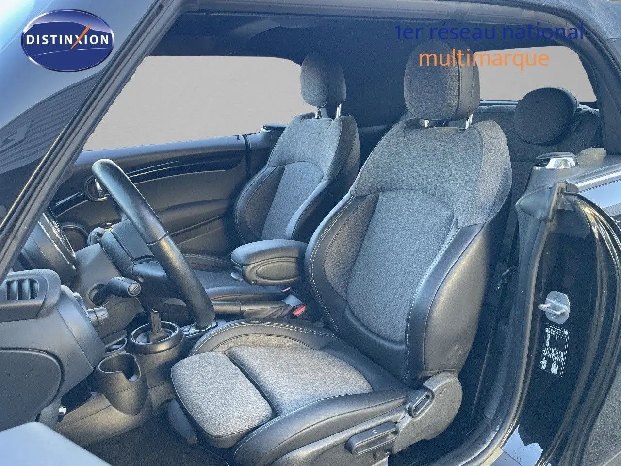 Vue intérieure côté conducteur de la MINI Cabriolet noire, mettant en valeur les sièges tissu gris et cuir noir.