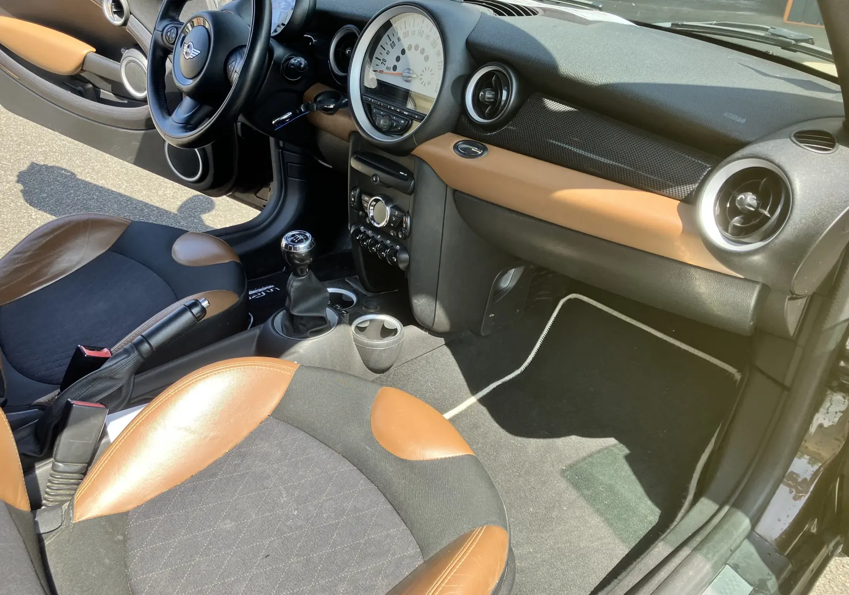 Intérieur avant droit d'une MINI Cooper S R56 2012 marron, sièges bi-ton cuir et tissu, tableau de bord noir et marron.