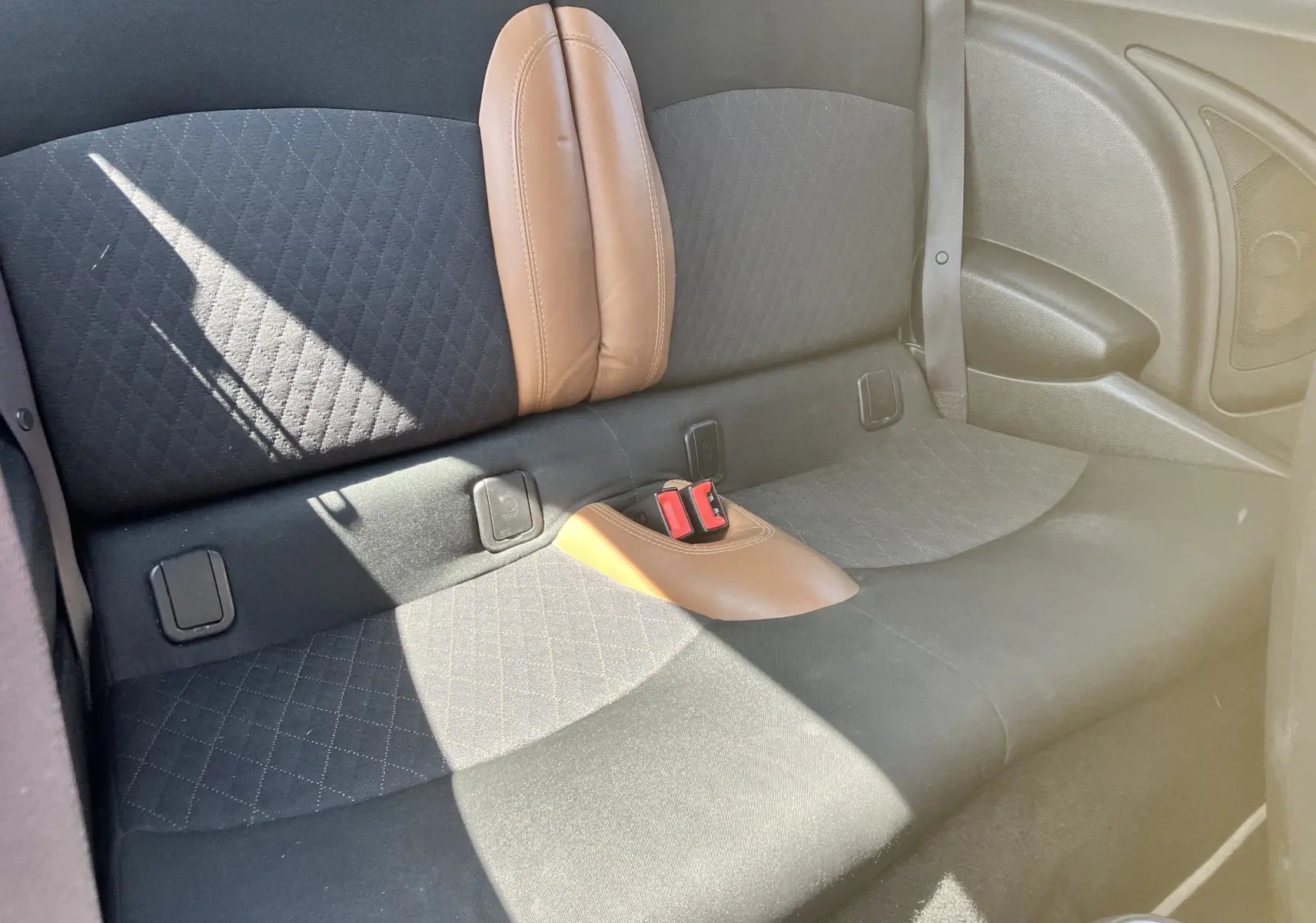 Vue intérieure du siège arrière de la MINI Cooper S R56 2012, tissu noir avec inserts marron et ceinture de sécurité visible.