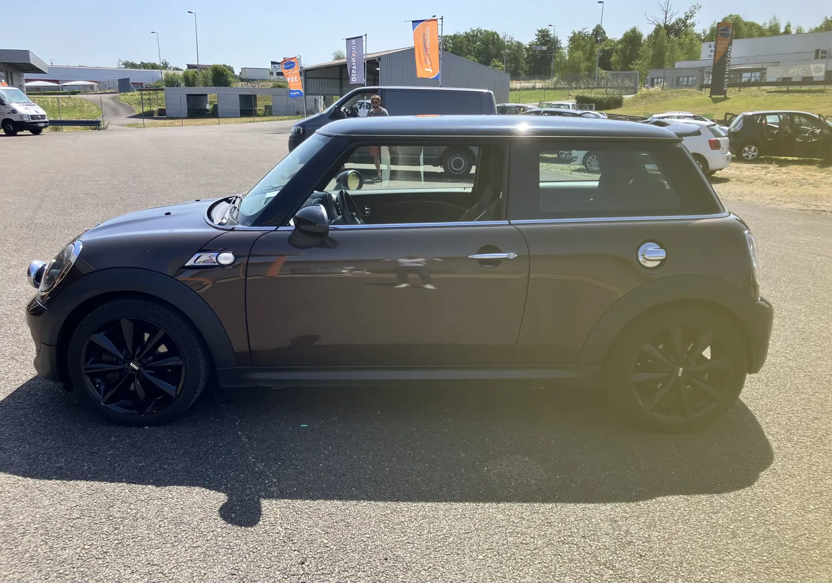 Profil côté gauche d'une MINI Cooper S R56 marron de 2012 avec jantes noires et toit noir sur parking extérieur.