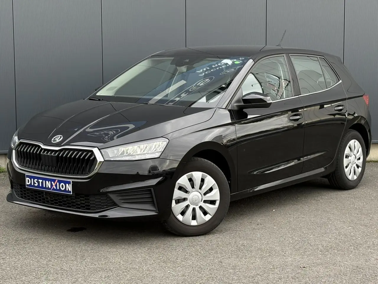 Vue 3/4 avant droite d’une SKODA FABIA 2024 noire Magic avec calandre chromée et jantes acier sur parking.