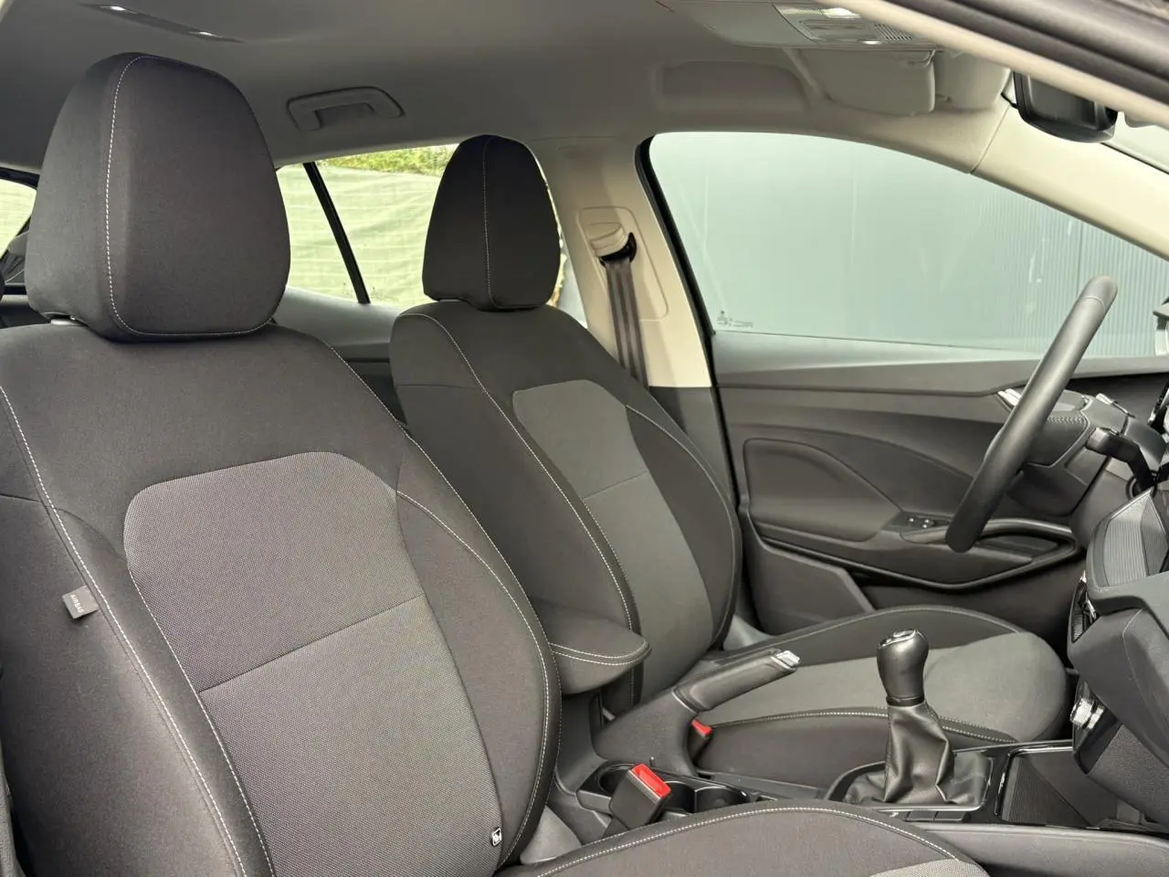 Vue intérieure côté conducteur de la Skoda Fabia 2024 noire, volant cuir, écran tactile et levier de vitesses manuel visibles.