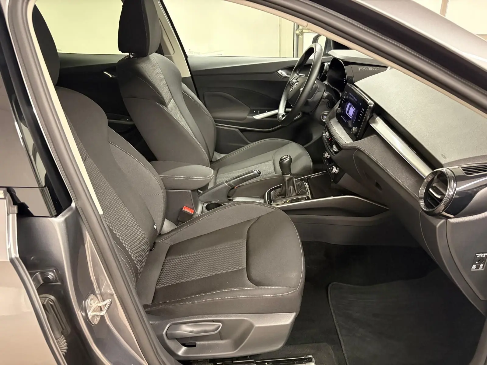 Vue intérieure côté conducteur de la Skoda Fabia 2023 gris graphite, avec sièges tissu et boîte manuelle visible.