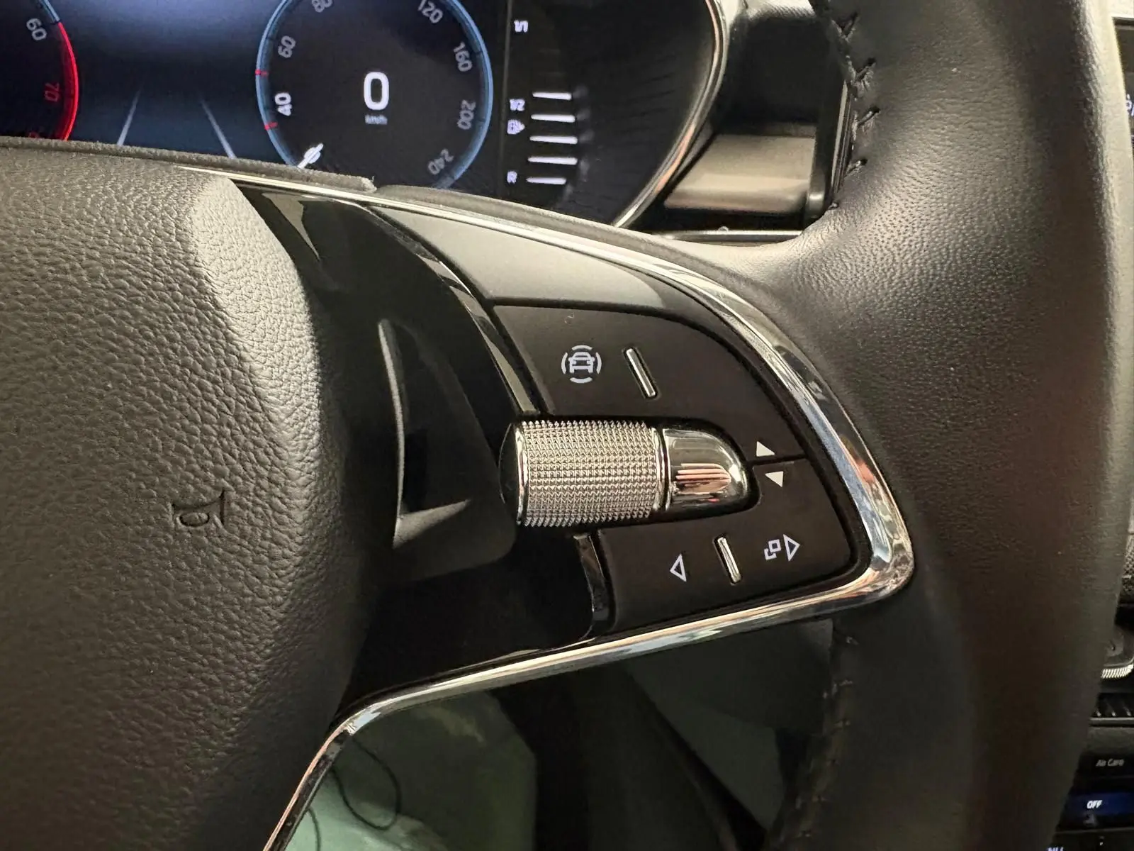 Gros plan sur les commandes gauche du volant en cuir noir de la Skoda Fabia 2023, avec molette métallique et boutons noirs.