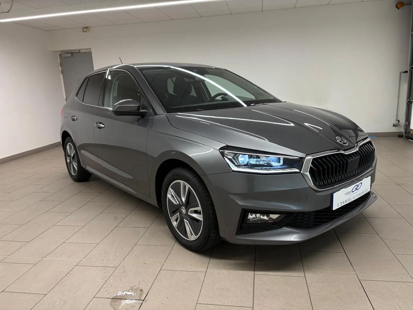 Skoda Fabia 2023 gris graphite métallisé vue 3/4 avant droit avec phares LED allumés en intérieur.