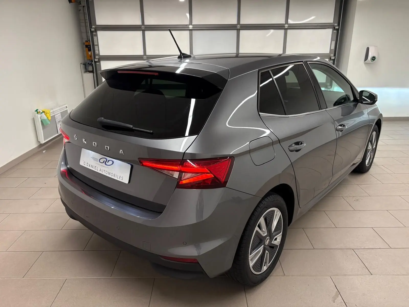 Vue 3/4 arrière droite d'une Skoda Fabia 2023 gris graphite métallisé, avec feux arrière allumés en intérieur.