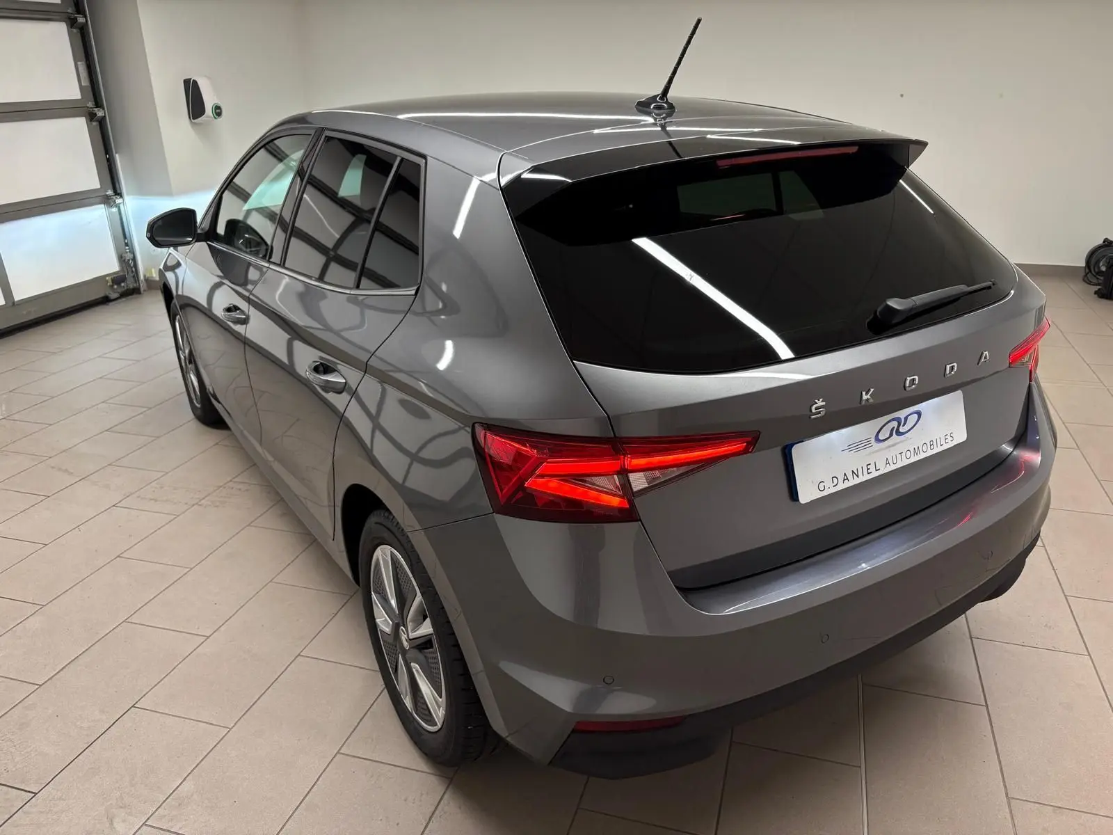 Vue 3/4 arrière droite d'une Skoda Fabia 2023 gris graphite métallisé avec vitres teintées et feux arrière allumés.