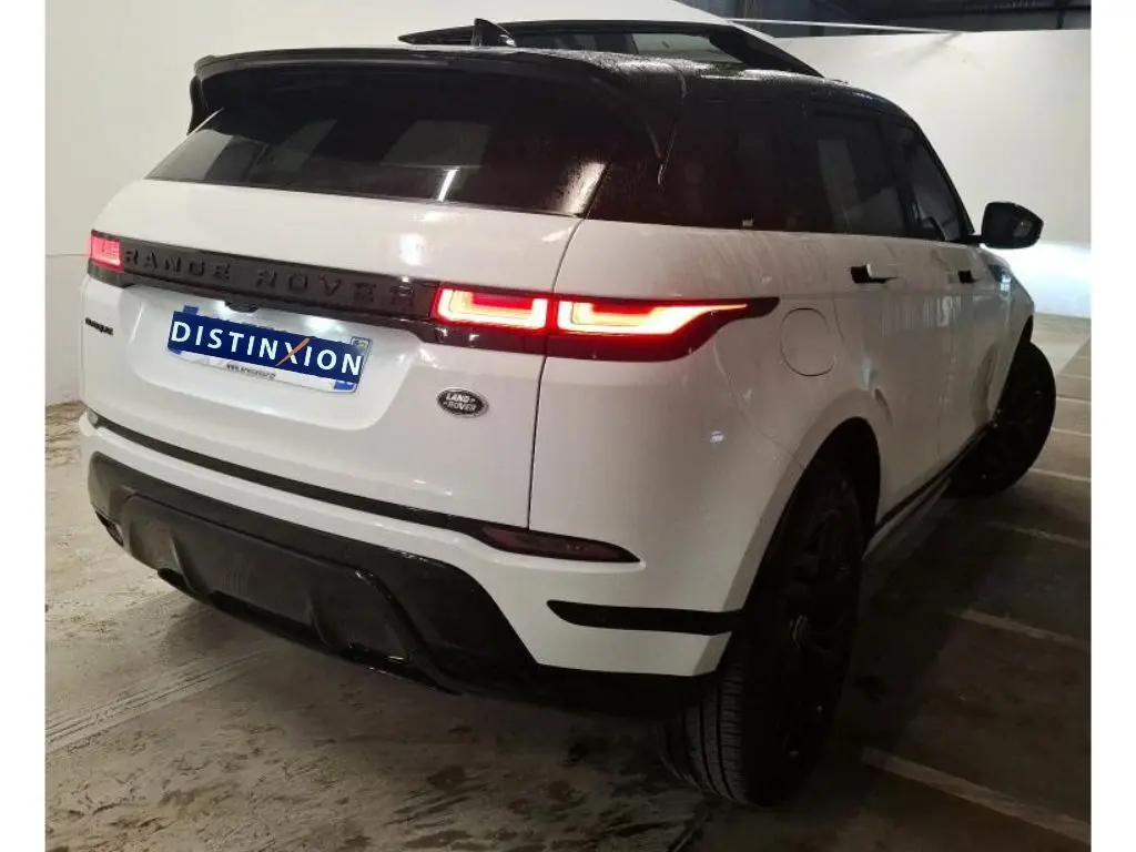 Vue 3/4 arrière droite d'un Range Rover Evoque blanc avec toit noir, feux arrière allumés et jantes noires.