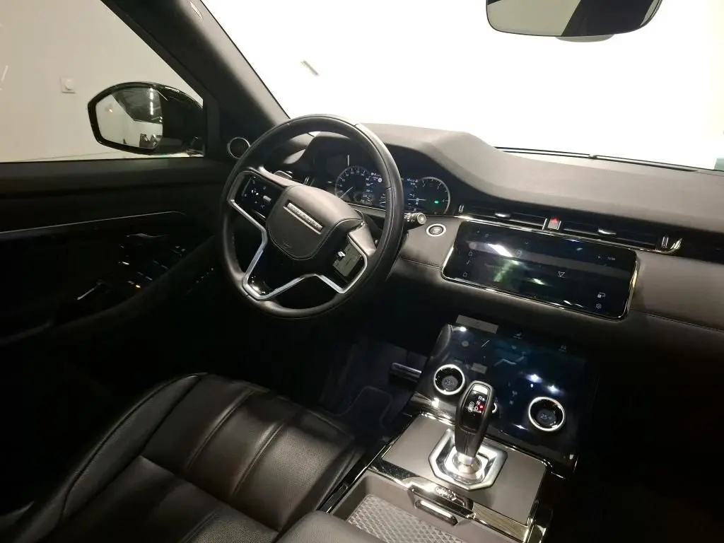 Vue intérieure côté conducteur du Range Rover Evoque 2022, avec volant cuir perforé et écran tactile central noir.