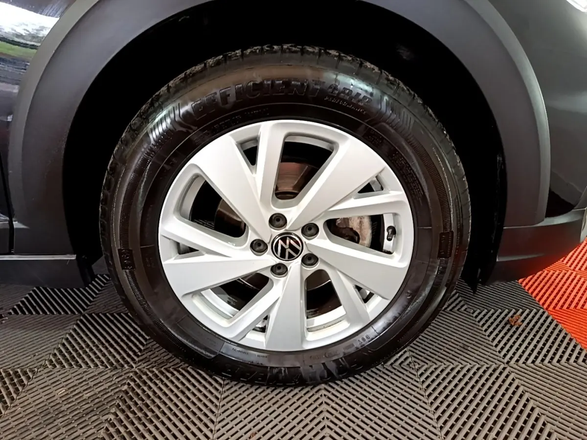 Gros plan sur la roue avant droite d’un Volkswagen Taigo noir, avec jante alliage argentée et logo VW central.