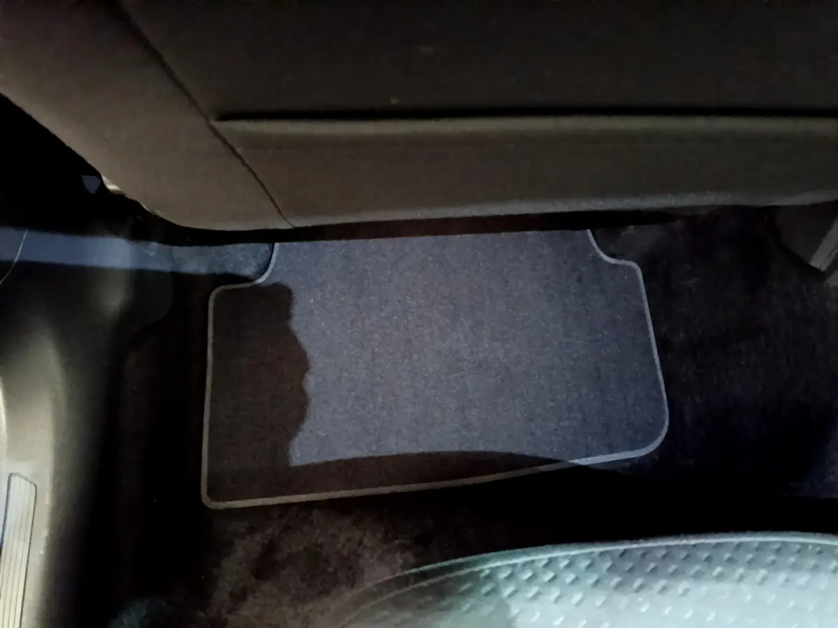 Vue intérieure du plancher côté passager avant avec tapis gris et partie inférieure de la planche de bord visible