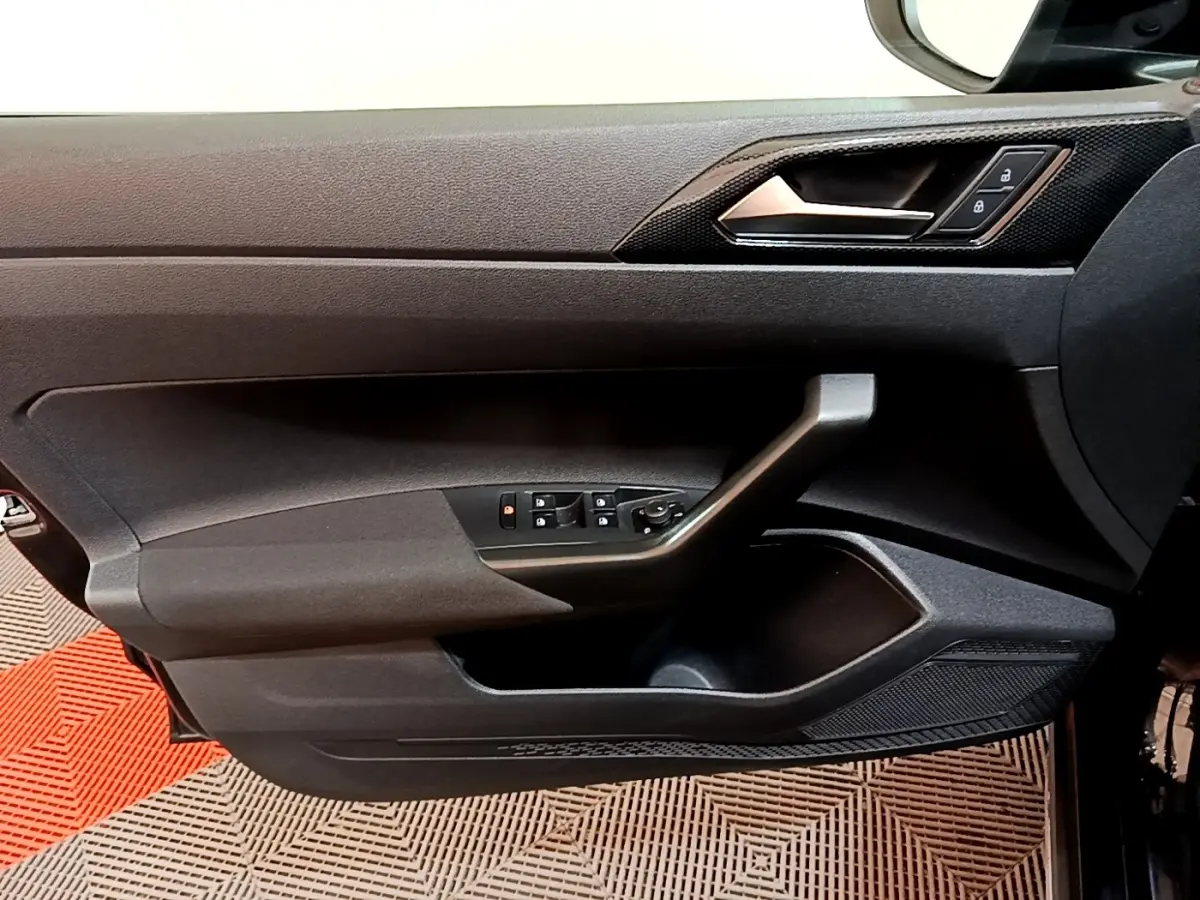 Vue intérieure du panneau de porte avant gauche noir du Volkswagen Taigo 2023 avec commandes électriques et poignée intégrée.