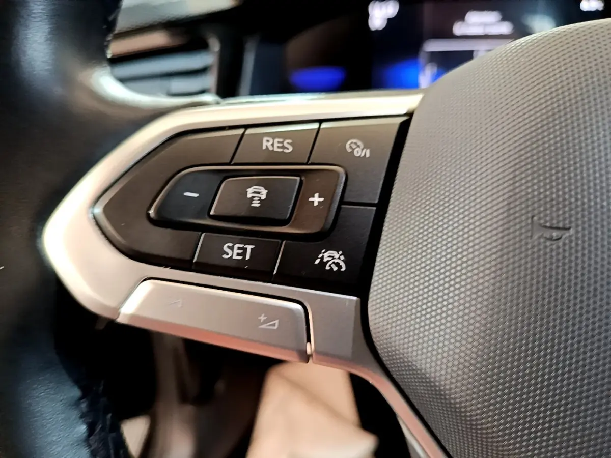 Gros plan sur les commandes du volant alu et cuir du Volkswagen Taigo noir, avec boutons de régulateur de vitesse.