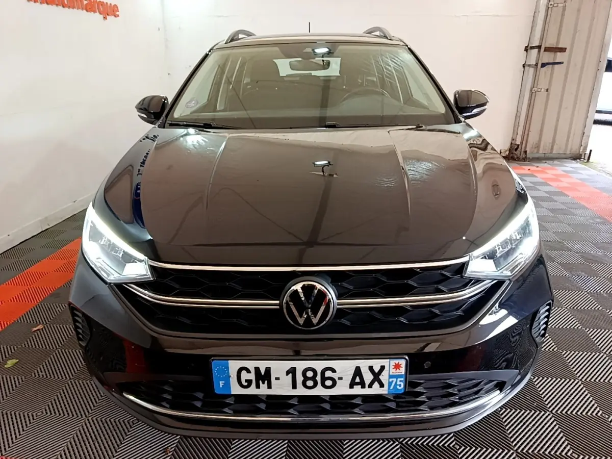 Vue avant d’un Volkswagen Taigo noir 2023 avec phares LED allumés dans un garage.