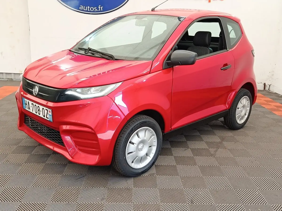Vue 3/4 avant d'une Aixam Ambition 0.5 City Pack rouge 2024 avec rétroviseur côté conducteur noir.