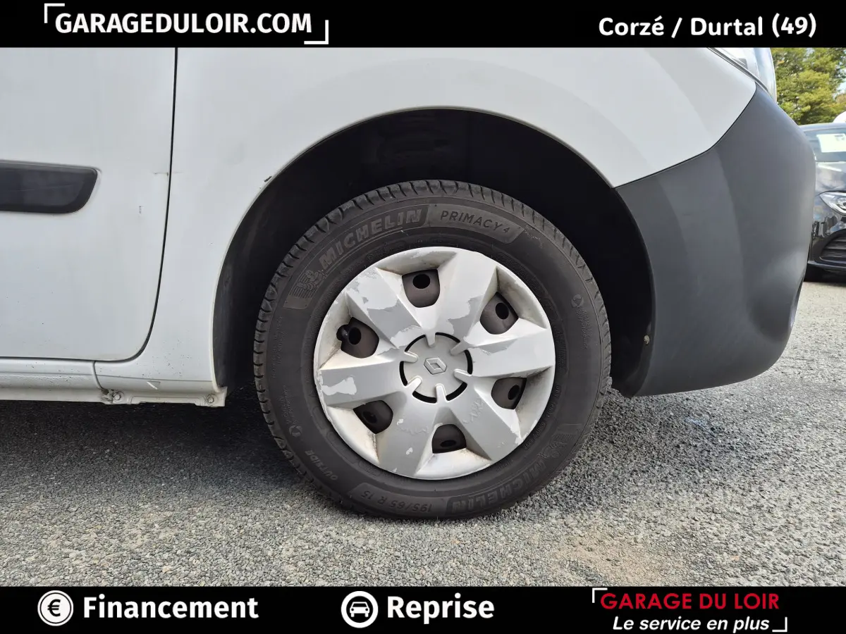 Gros plan sur la roue avant droite d’un Renault Kangoo blanc avec enjoliveur usé et pare-chocs noir.