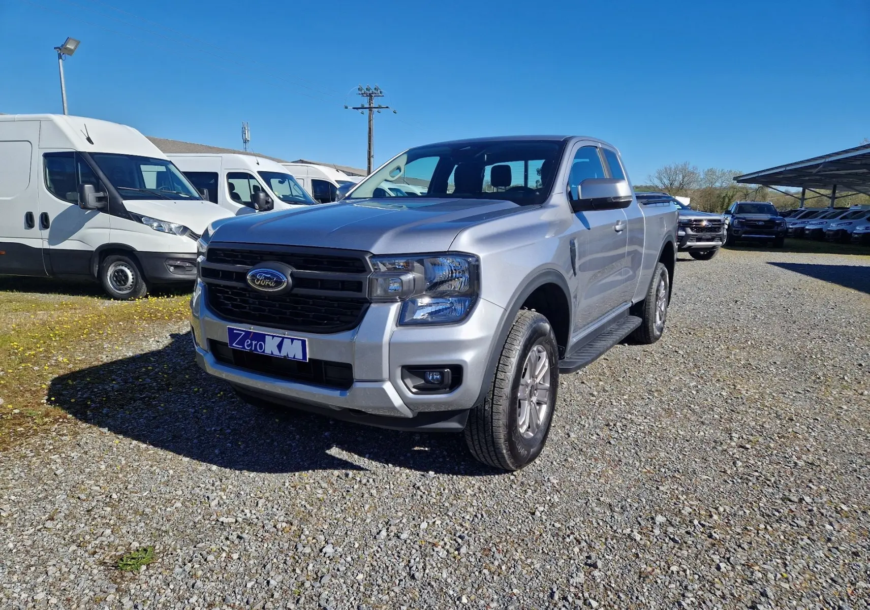 Ford Ranger Super Cabine gris Iconic vu en 3/4 avant droit sur un parking extérieur par temps clair.