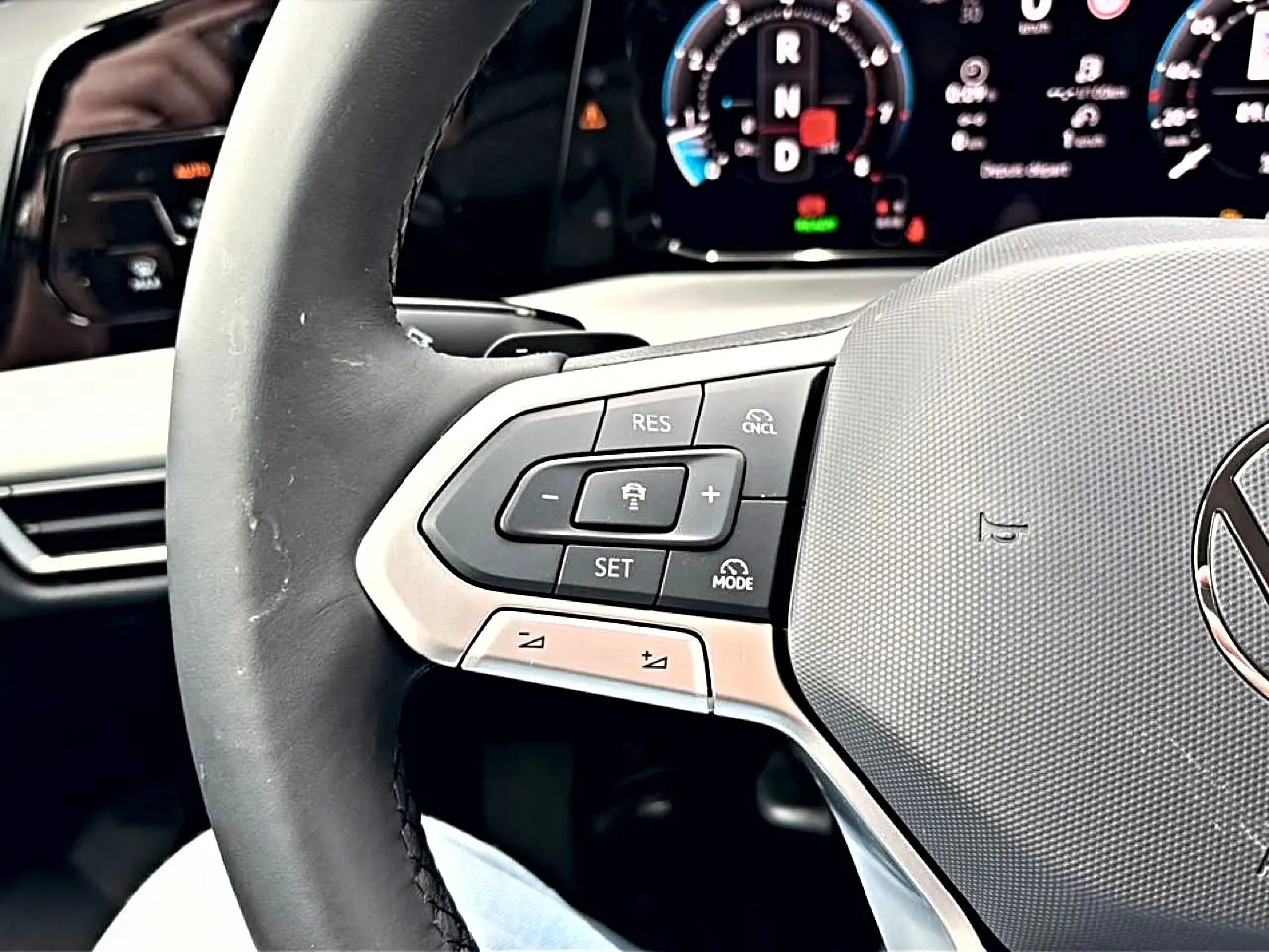 Gros plan sur le volant noir de la Volkswagen Golf 2026, avec commandes intégrées et tableau de bord digital en arrière-plan.
