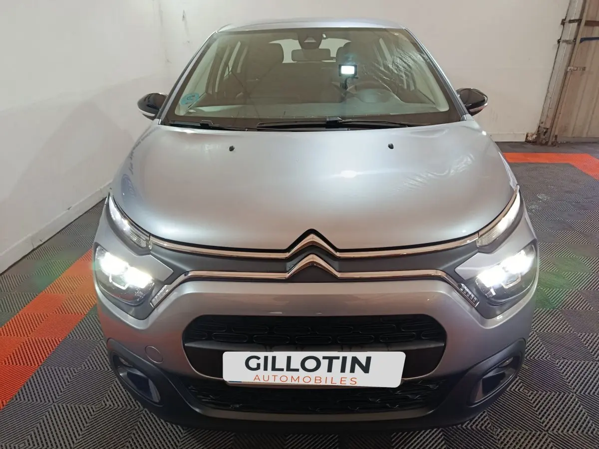 Vue frontale d'une Citroën C3 gris clair 2024 avec phares LED allumés dans un garage fermé.