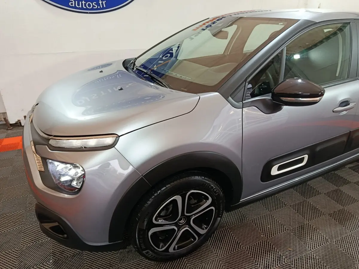 Vue 3/4 avant droit d'une Citroën C3 gris clair avec phares LED et jantes alliage noires distinctives.