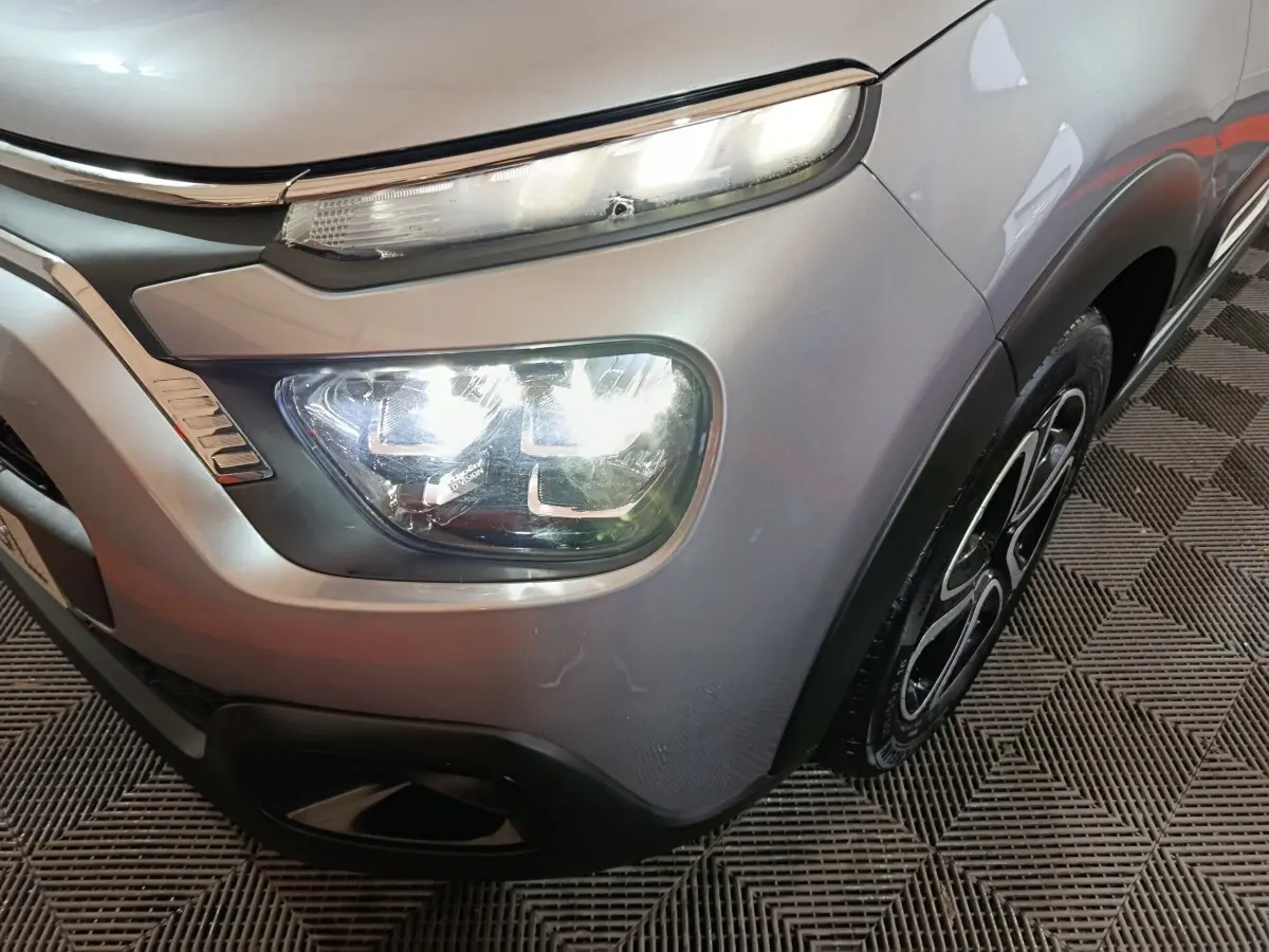 Gros plan sur l'avant droit gris clair d'une Citroën C3 2024 avec phares LED allumés et jante noire stylisée.